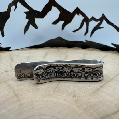 U.S. Morgan Dollar Silver Coin Money Clip on a light wood round with a hand cut metal mountain background.
- Mountainstruck Coin Jewelry