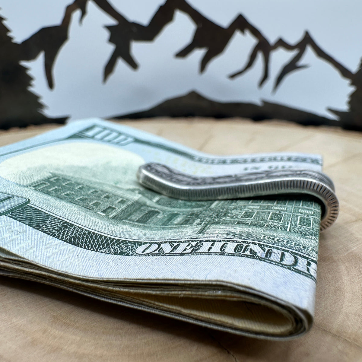 U.S. Morgan Dollar Silver Coin Money Clip holding money on a light wood round with a hand cut metal mountain background.
- Mountainstruck Coin Jewelry