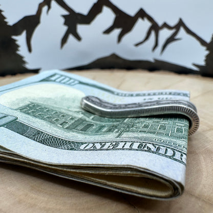 U.S. Morgan Dollar Silver Coin Money Clip holding money on a light wood round with a hand cut metal mountain background.
- Mountainstruck Coin Jewelry