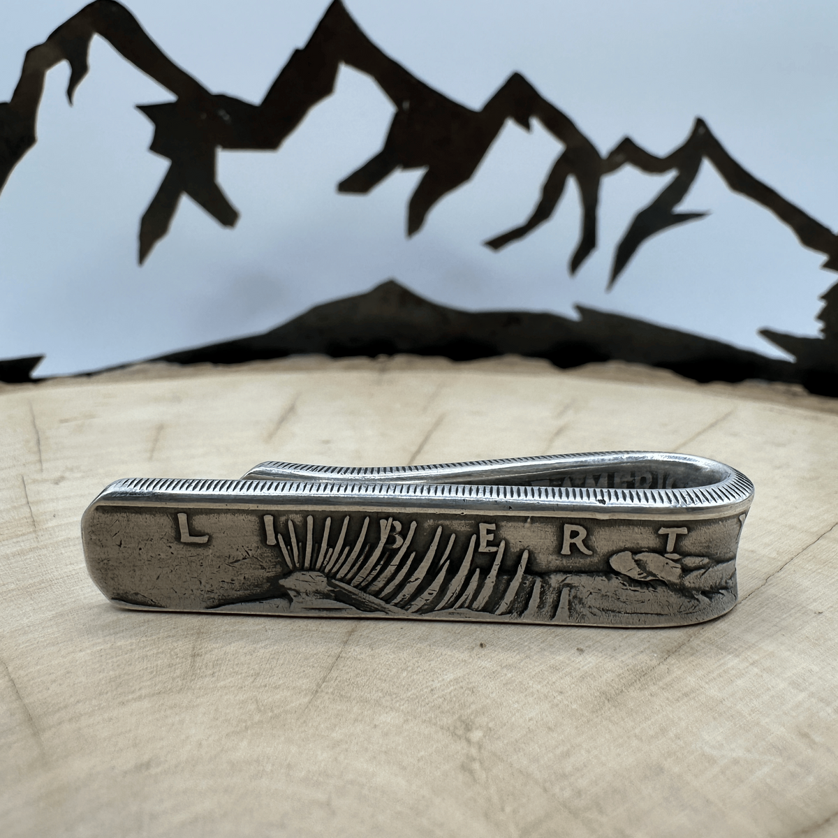 U.S. Peace Dollar Silver Coin Money Clip on a light wood round with a hand cut metal mountain background.
- Mountainstruck Coin Jewelry
