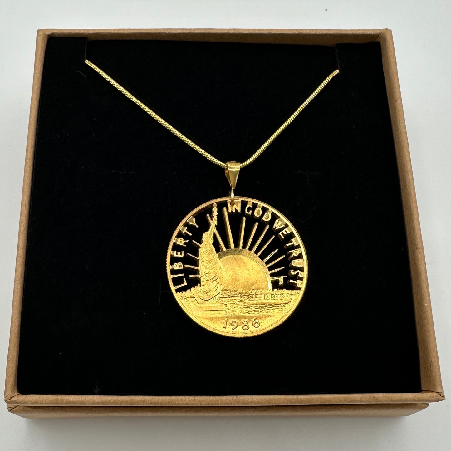 24k Plate U.S. Nation of Immigrants Cut Half Dollar Coin Necklace in a brown kraft box on a black velvet background. - Mountainstruck Coin Jewelry