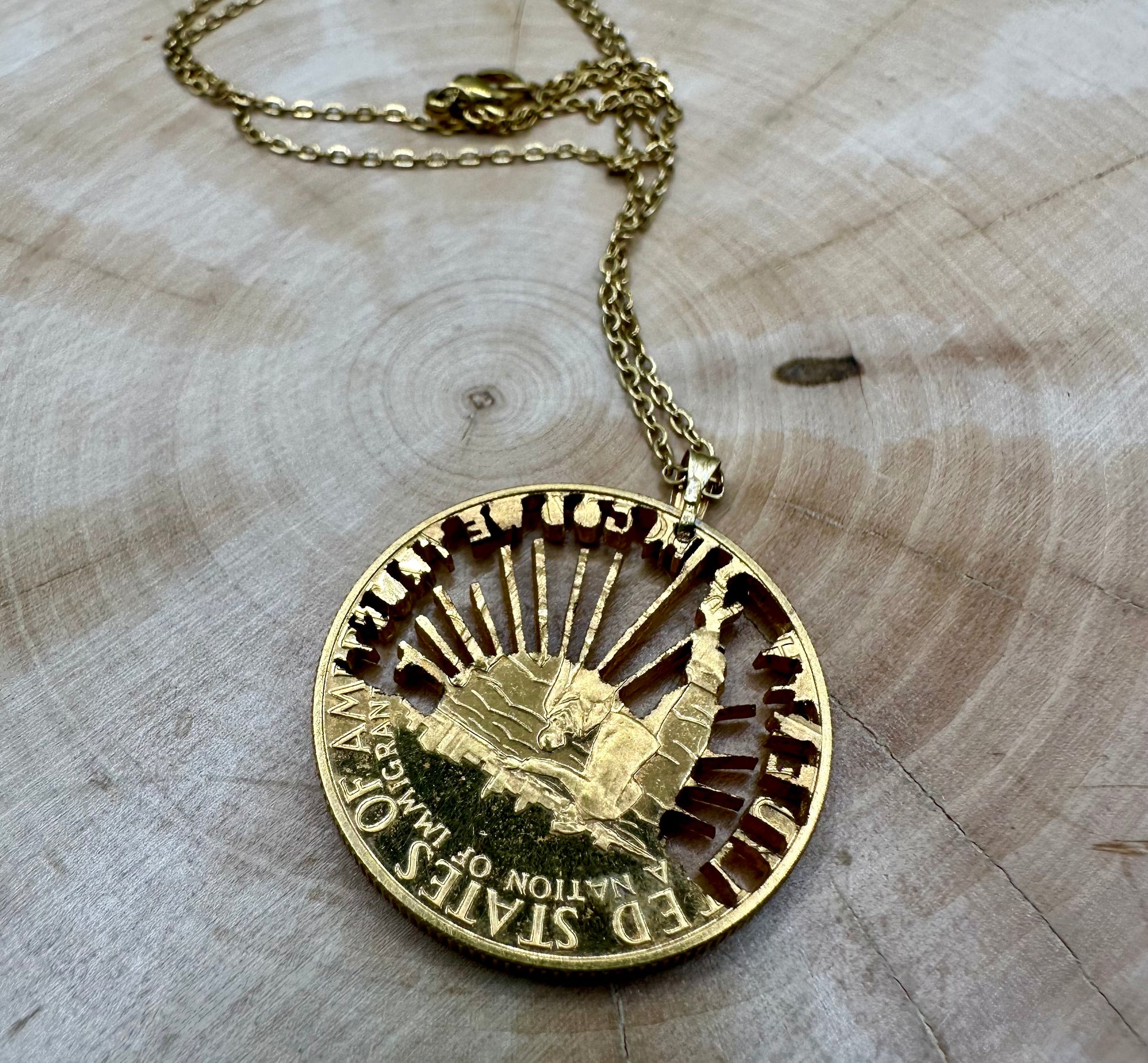 24k Plate U.S. Nation of Immigrants Half Dollar Hand Cut Coin Necklace on a light wood round. - Mountainstruck Coin Jewelry