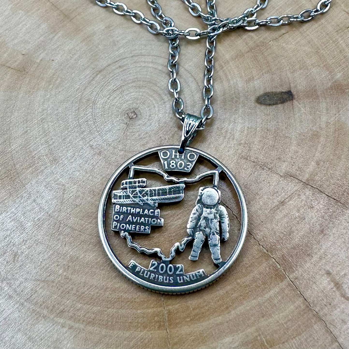 U.S. Ohio State Quarter Hand Cut Coin Necklace with a stainless steel chain on a wood background. - Mountainstruck Coin Jewelry