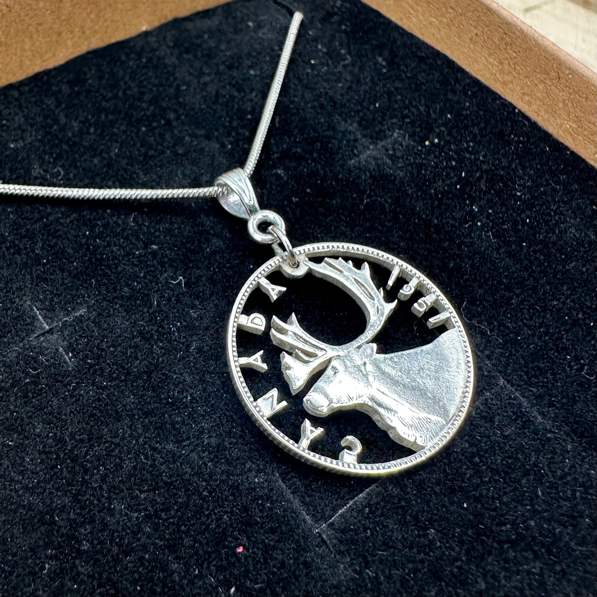 Caribou Canada Silver 25 Cent Hand Cut Coin Necklace on a black velvet  background in a brown kraft box. - Mountainstruck Coin Jewelry