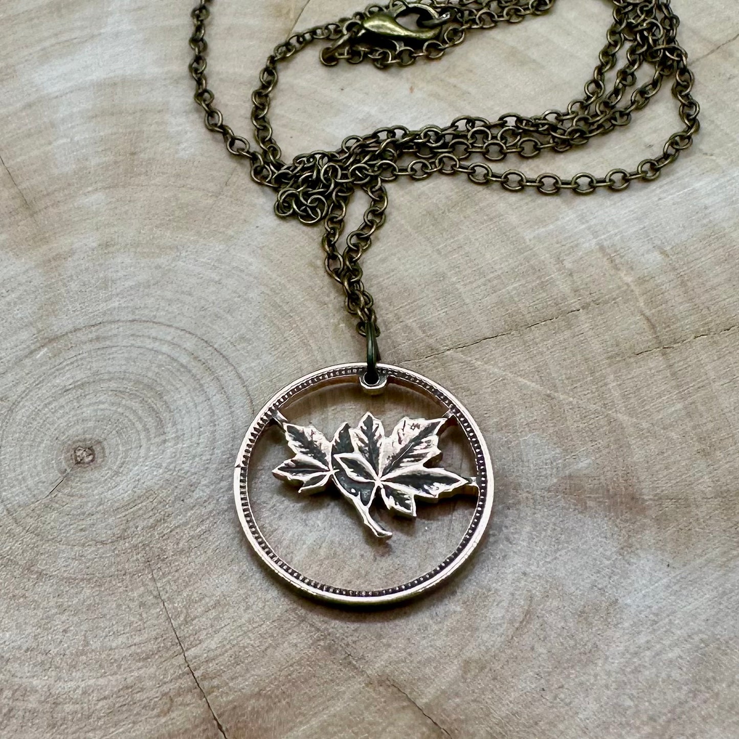 Canada Maple Leaf Penny Hand Cut Coin Necklace with bronze chain on a light wood round. - Mountainstruck Coin Jewelry