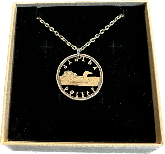 Canadian Loonie 1 Dollar Hand Cut Coin Necklace with stainless chain in a brown kraft box on a black velvet background. - Mountainstruck Coin Jewelry