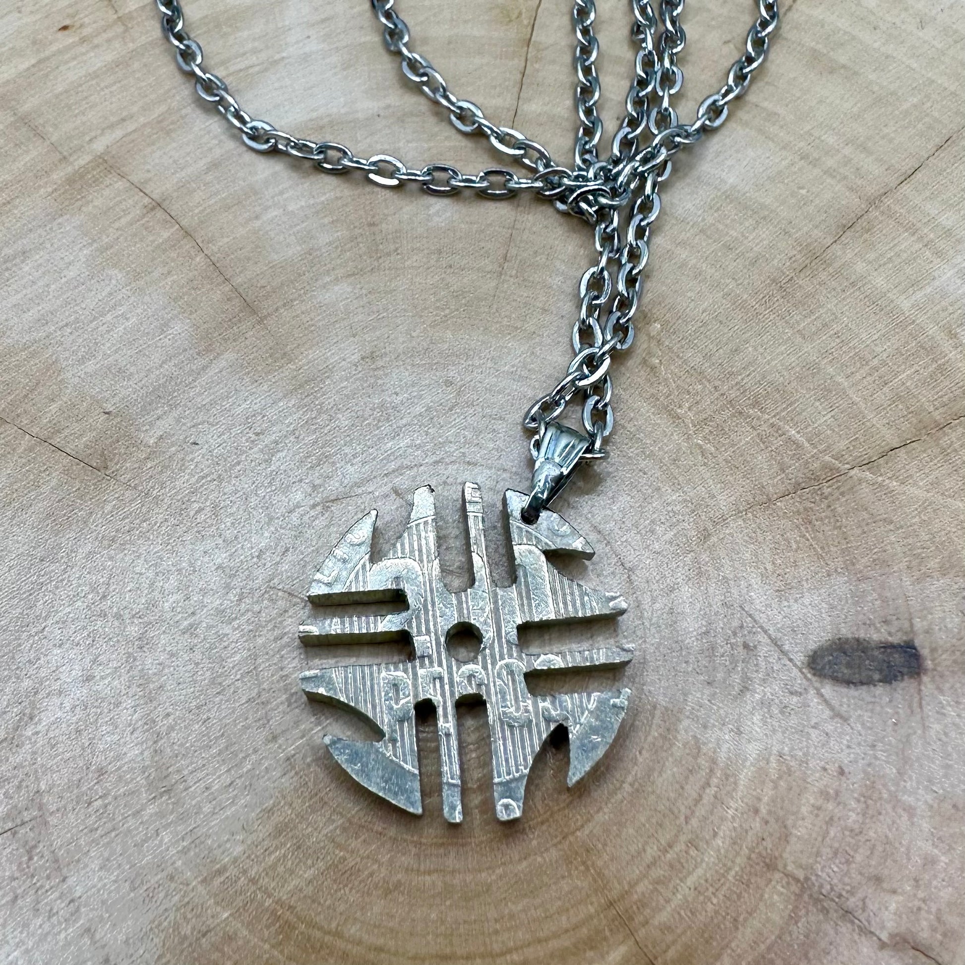 Columbia 200 Pesos Quimbaya Spindle Wheel Hand Cut Coin Necklace back with a stainless chain on a light wood round. - Mountainstruck Coin Jewelry