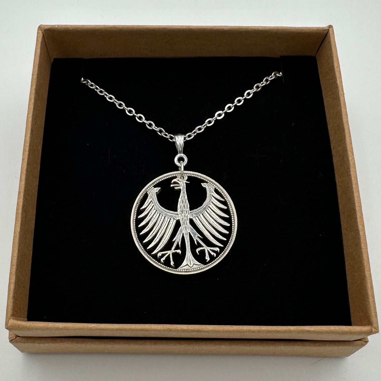 Germany Eagle 5 Mark Hand Cut Silver Coin Necklace in a brown kraft box on a black velvet background. - Mountainstruck Coin Jewelry