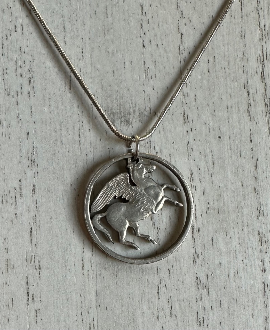 Greece Pegasus 5 Drachmai Hand Cut Coin Necklace with snake chain on a white wood background. - Mountainstruck Coin Jewelry