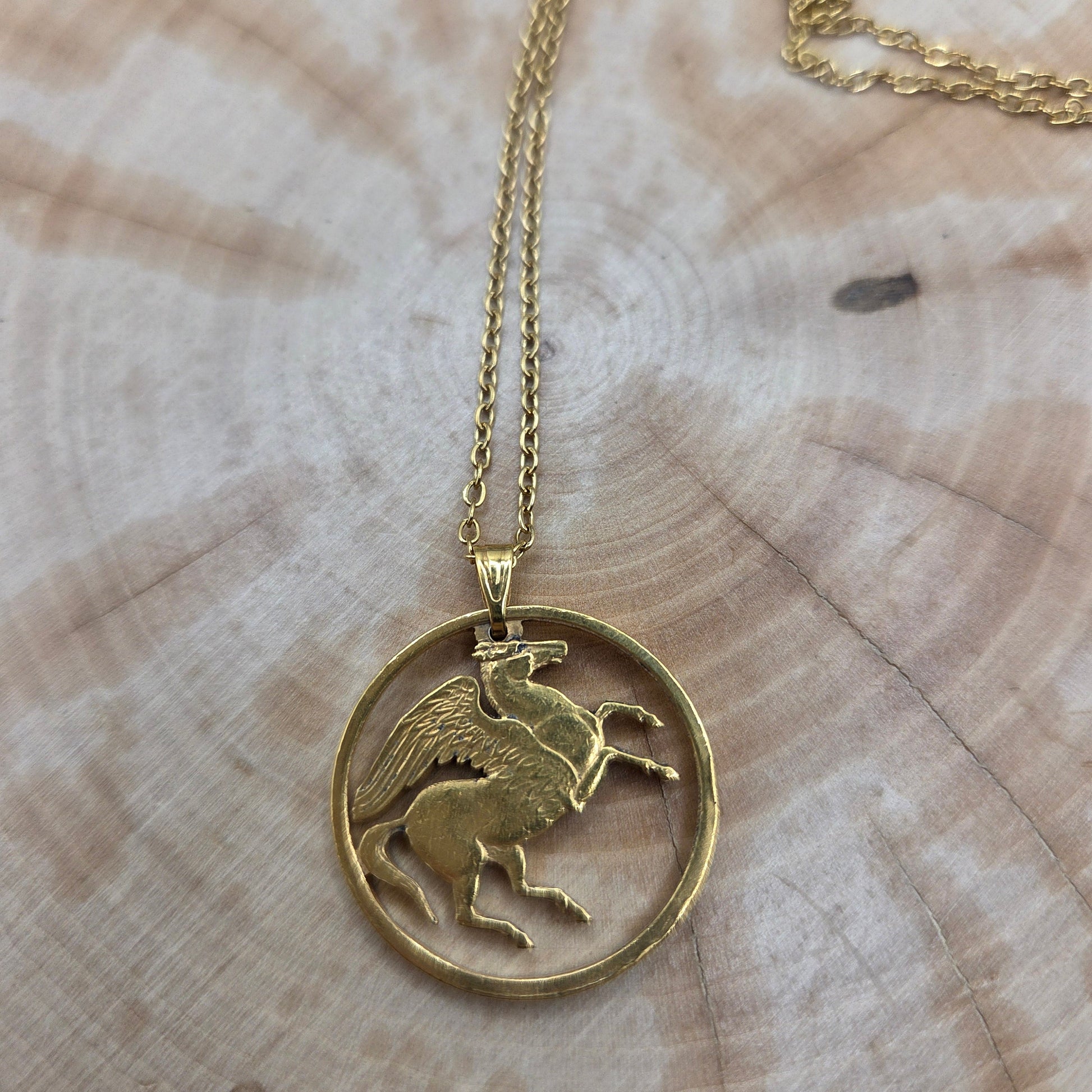 Greece Pegasus 5 Drachmai Hand Cut Coin Necklace gold plated with a gold plated chain on a wood background. - Mountainstruck Coin Jewelry