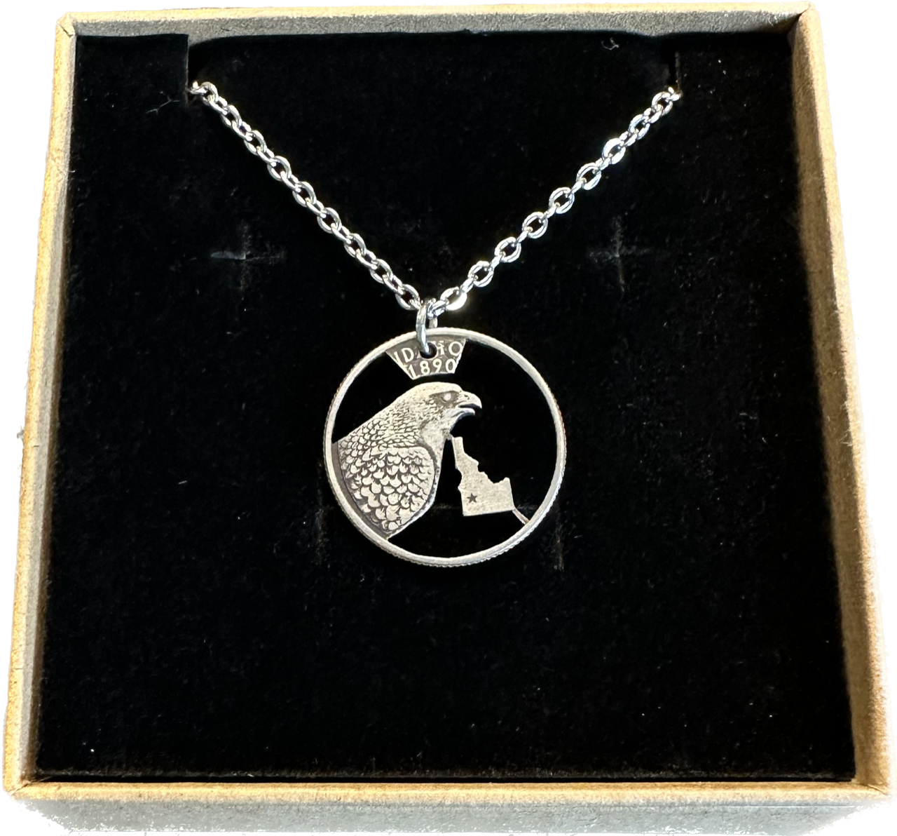 Idaho State Quarter Hand Cut Coin Necklace with a stainless chain in a brown kraft box on a black velvet background. - Mountainstruck Coin Jewelry