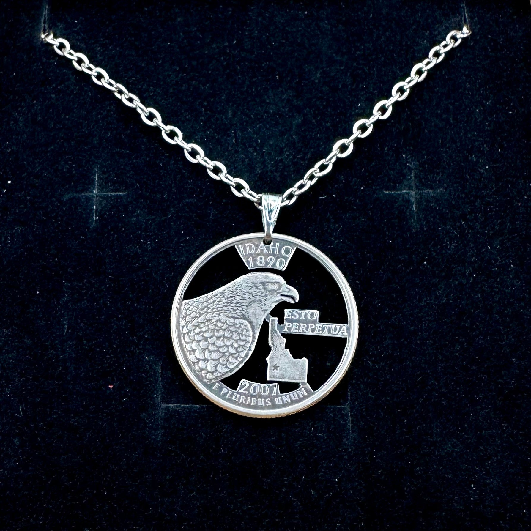 Idaho State Quarter Hand Cut Coin Necklace with a stainless chain on a black velvet background. - Mountainstruck Coin Jewelry