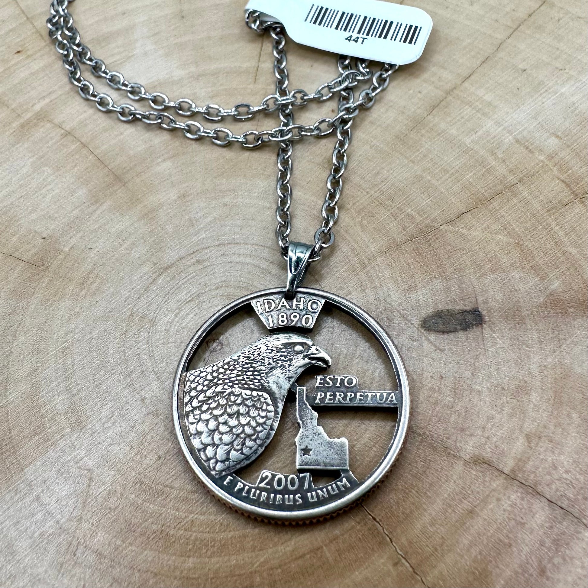 Idaho State Quarter Hand Cut Coin Necklace with a stainless steel chain on a wood background. - Mountainstruck Coin Jewelry