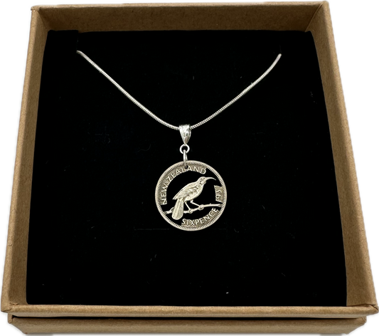 Huia Bird Silver New Zealand 6 Pence Hand Cut Coin Necklace in a brown kraft box on a black velvet background. - Mountainstruck Coin Jewelry