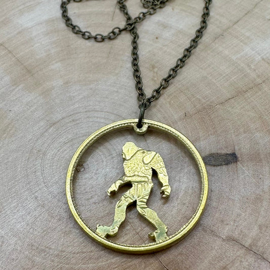Sasquatch Hand Cut Token Necklace with a bronze chain on a light wood background. - Mountainstruck Coin Jewelry