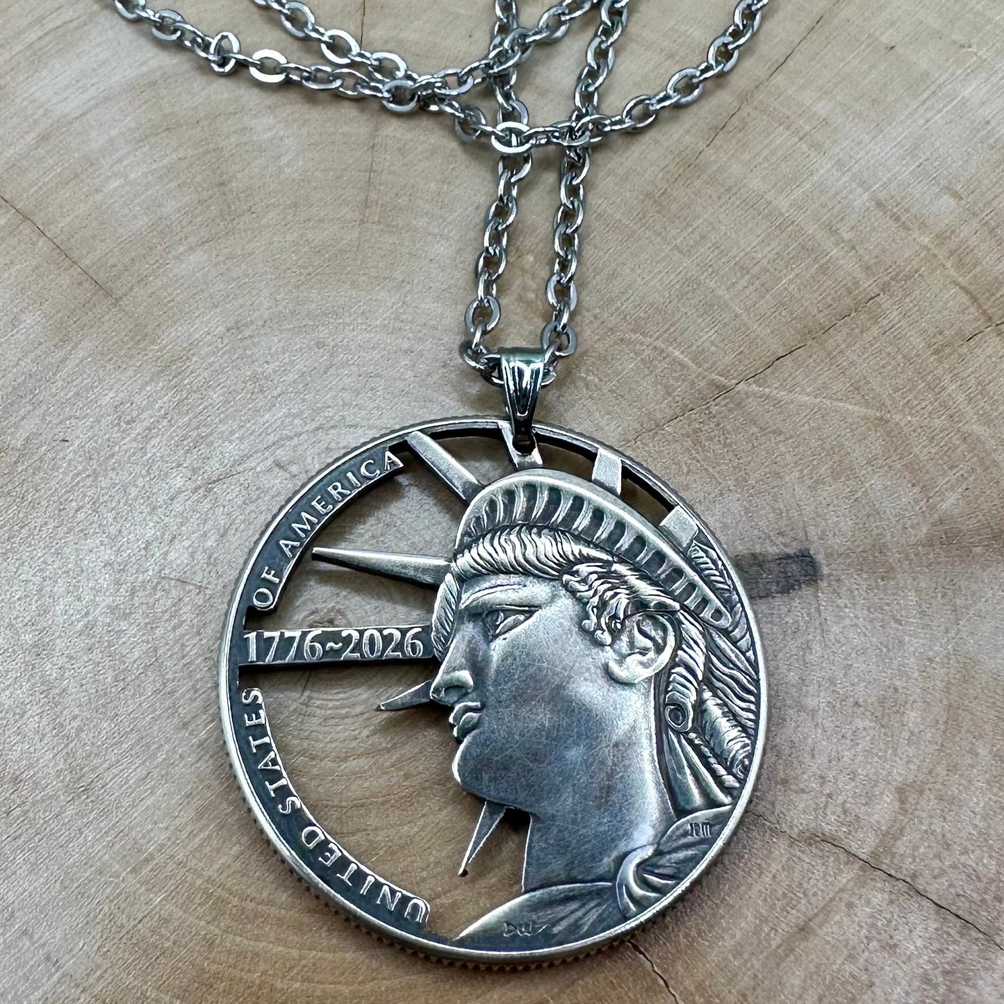 U.S. Half Dollar Hand Cut Coin Necklace (front) with a stainless chain on a light wood background. - Mountainstruck Coin Jewelry