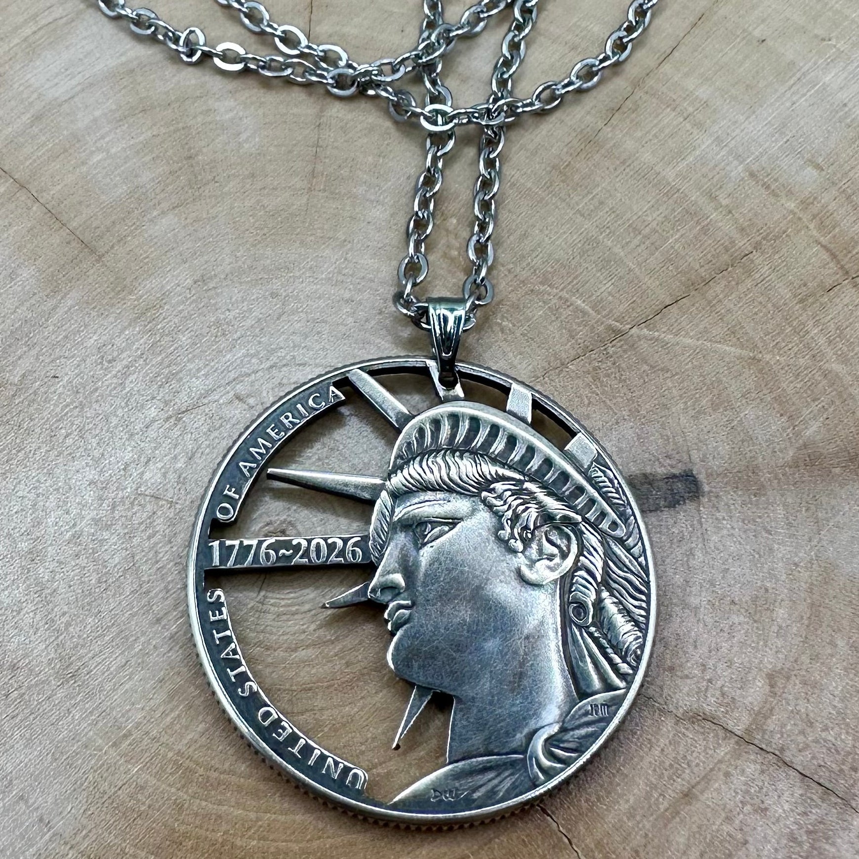 U.S. Half Dollar Hand Cut Coin Necklace (front) with a stainless chain on a light wood background. - Mountainstruck Coin Jewelry