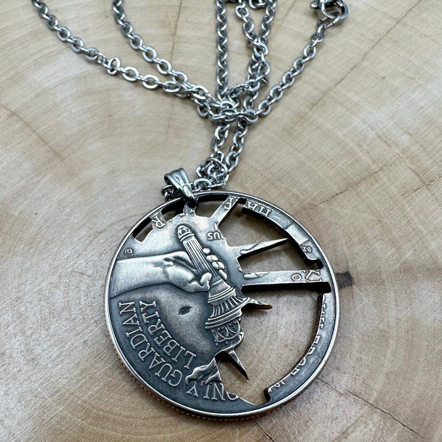 U.S. Half Dollar Hand Cut Necklace (front) with a stainless chain light wood background. - Mountainstruck Coin Jewelry