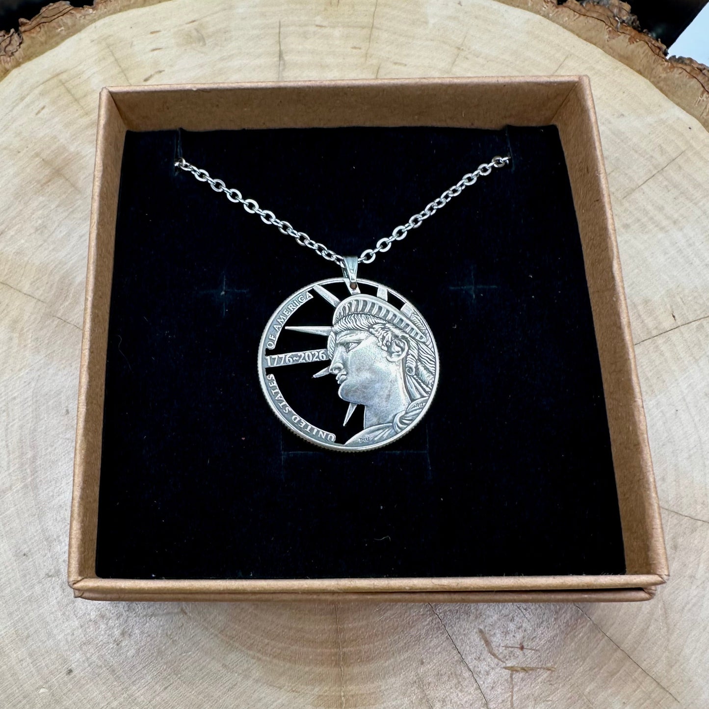 U.S. Half Dollar Hand Cut Coin Necklace (front) with a stainless chain on a black velvet background in a brown kraft box on a wood round. - Mountainstruck Coin Jewelry
