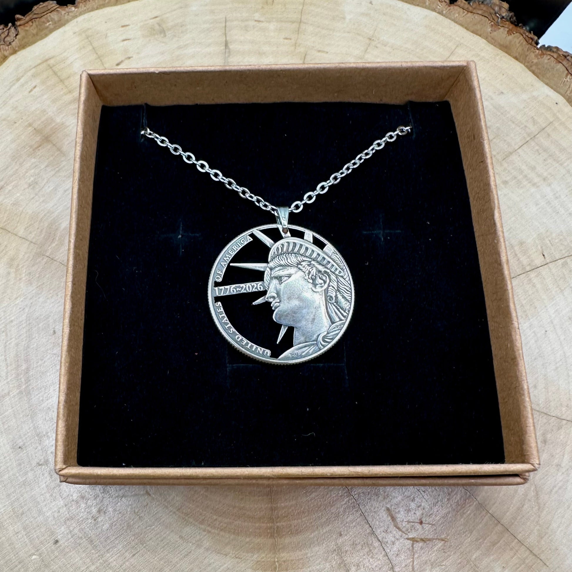 U.S. Half Dollar Hand Cut Coin Necklace (front) with a stainless chain on a black velvet background in a brown kraft box on a wood round. - Mountainstruck Coin Jewelry