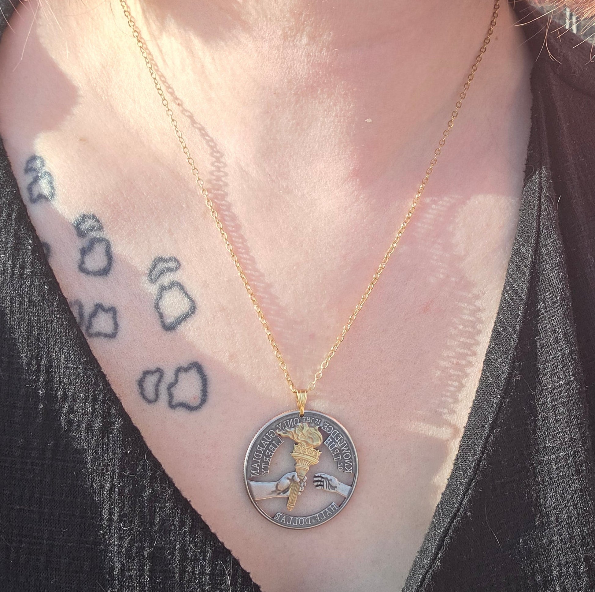 U.S. 2026 Half Dollar Hand Cut Coin Necklace (reverse) 24k gold plated torch with a gold plated chain on a persons neck with a black v-neck shirt and a small tattoo on collar bone. - Mountainstruck Coin Jewelry