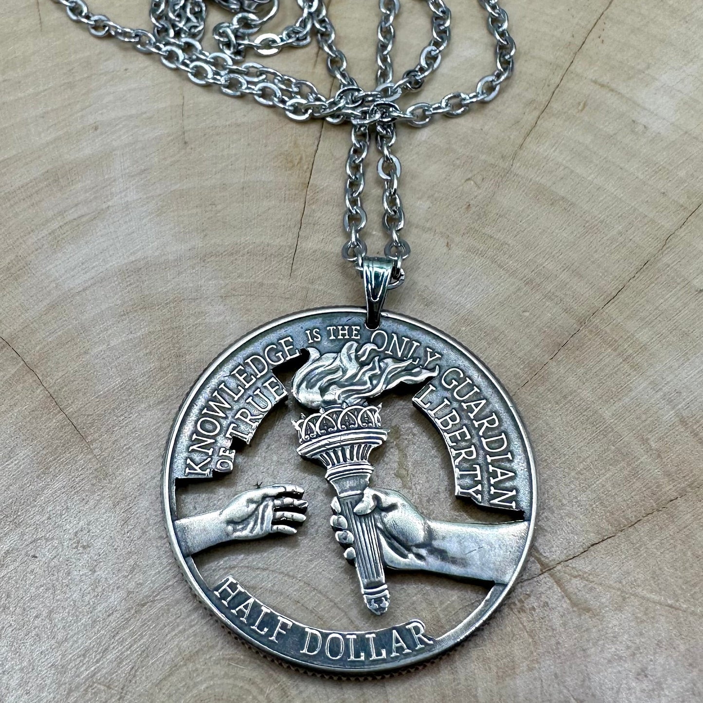 U.S. 2026 Half Dollar Hand Cut Coin Necklace (reverse) with a stainless chain on a light wood background. - Mountainstruck Coin Jewelry