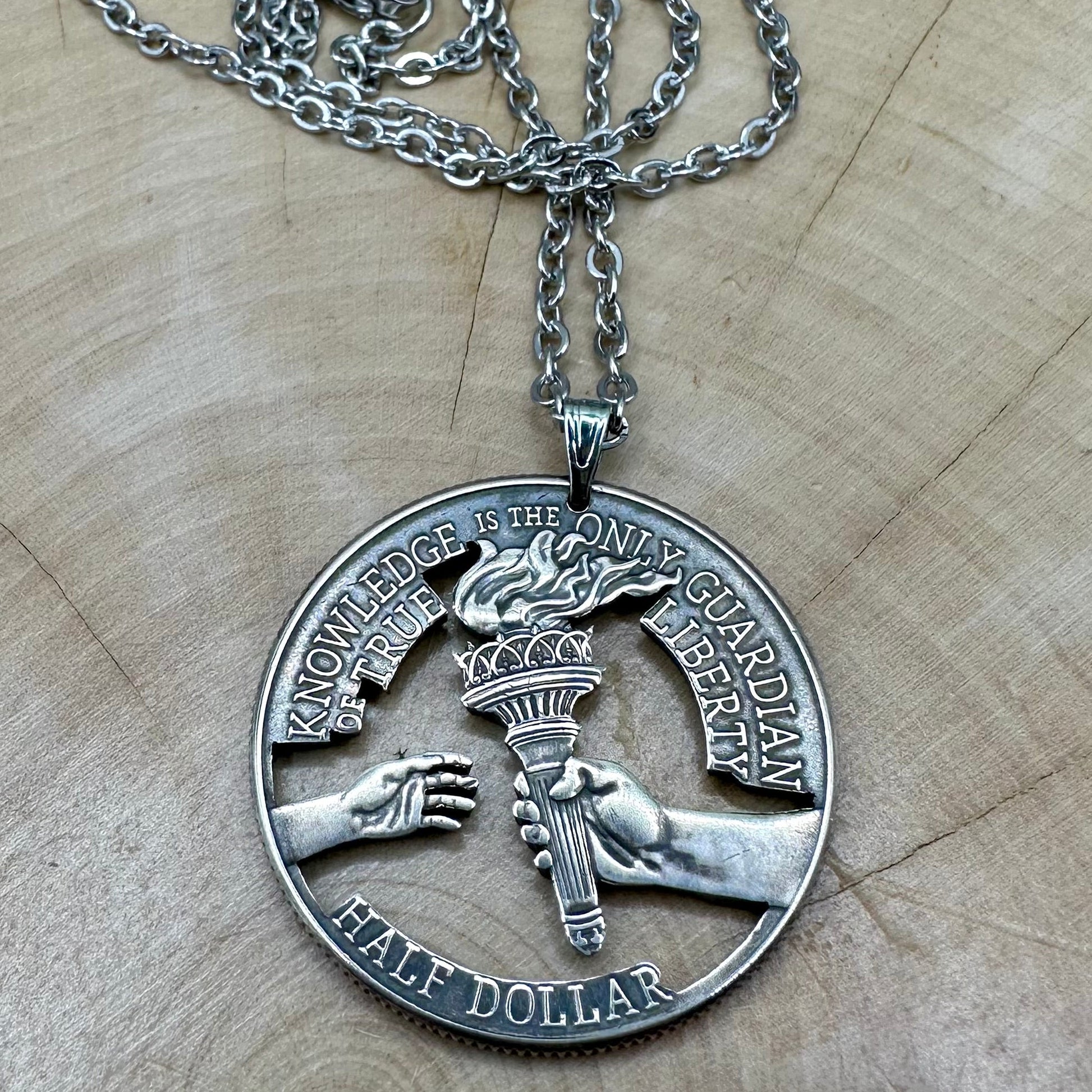 U.S. 2026 Half Dollar Hand Cut Coin Necklace (reverse) with a stainless chain on a light wood background. - Mountainstruck Coin Jewelry