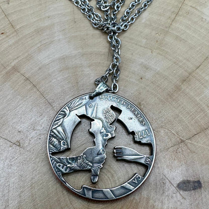 U.S. 2026 Half Dollar Hand Cut Coin Necklace (reverse) back with a stainless chain on a light wood background. - Mountainstruck Coin Jewelry