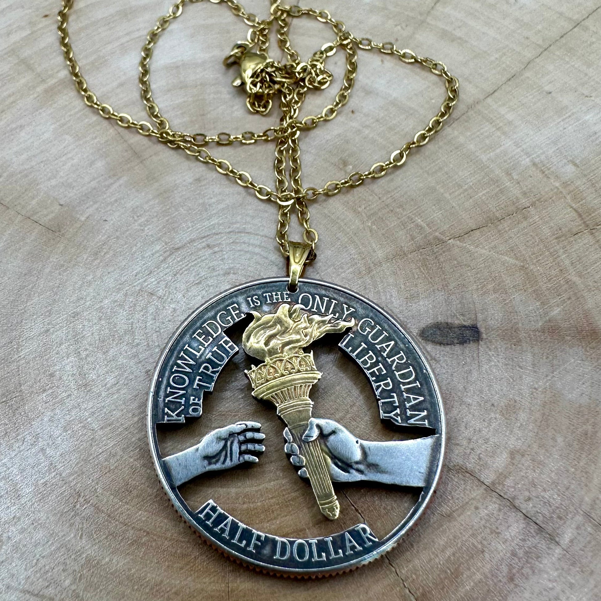 U.S. 2026 Half Dollar Hand Cut Coin Necklace (reverse) 24k gold plated torch with a gold plated chain on a light wood round. - Mountainstruck Coin Jewelry