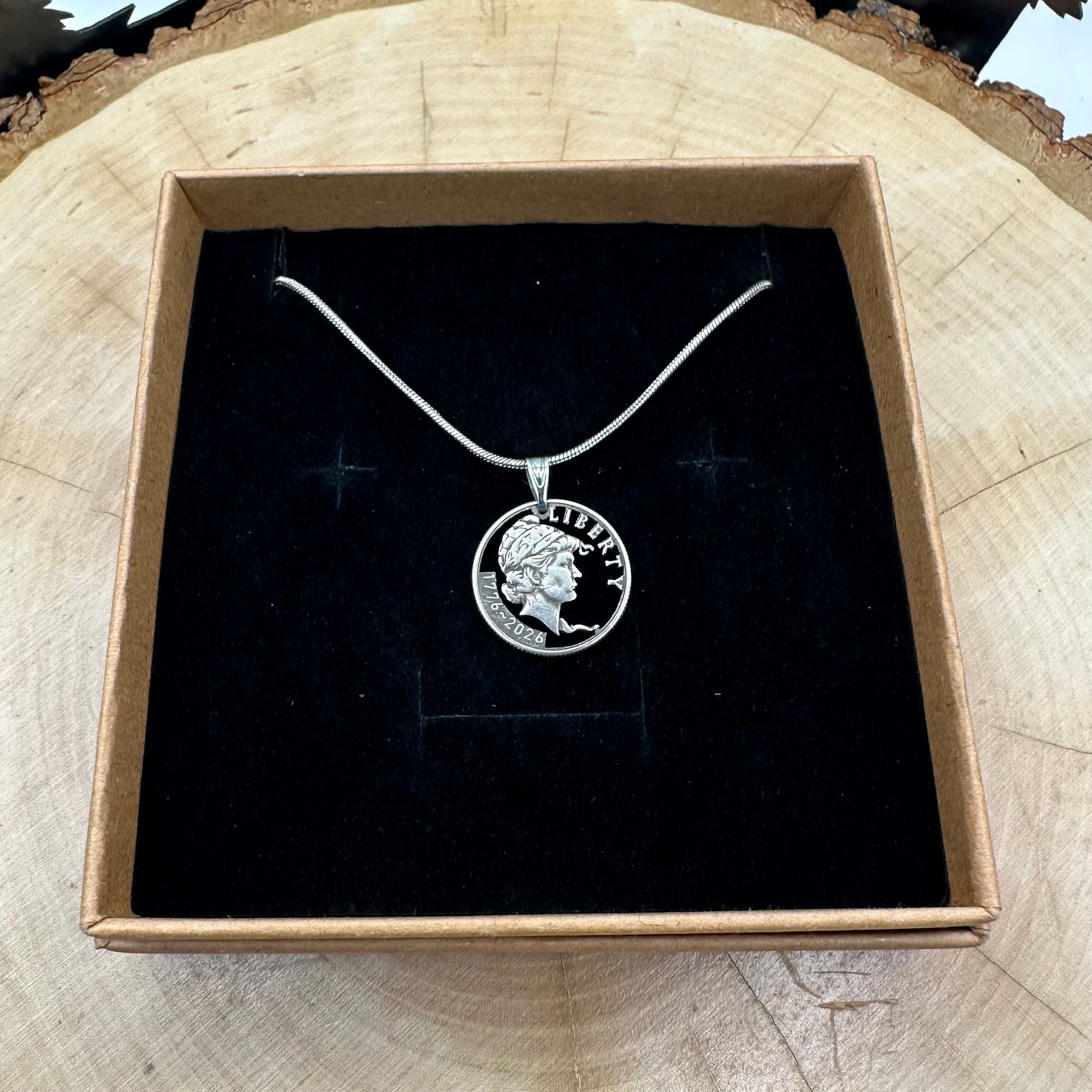 U.S. 2026 "Lady Liberty" Dime Hand Cut Coin Necklace on a black velvet background in a brown kraft box on a wood round. - Mountainstruck Coin Jewelry