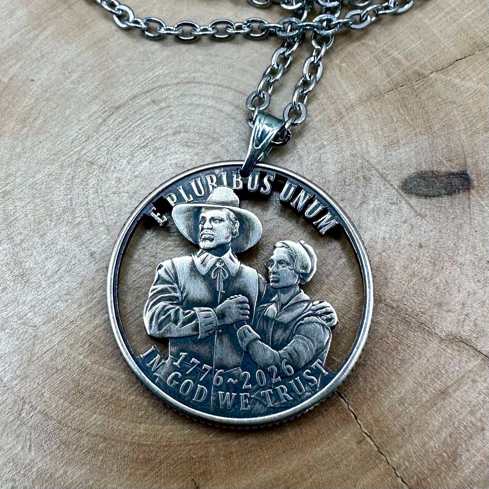 U.S. 2026 "Pilgrim" Quarter Hand Cut Coin Necklace with a stainless chain on a wood round. -Mountainstruck Coin Jewelry