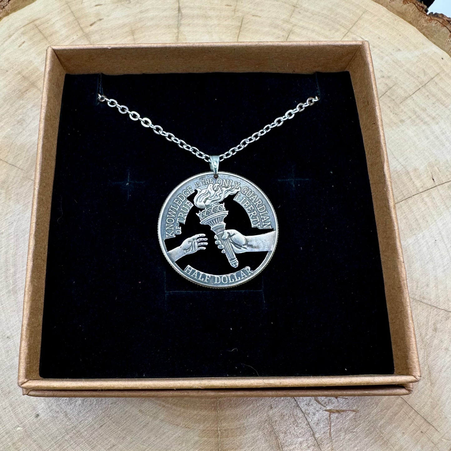 U.S. 2026 "Torch" Half Dollar Hand Cut Coin Necklace with a stainless chain on a black velvet background. - Mountainstruck Coin Jewelry