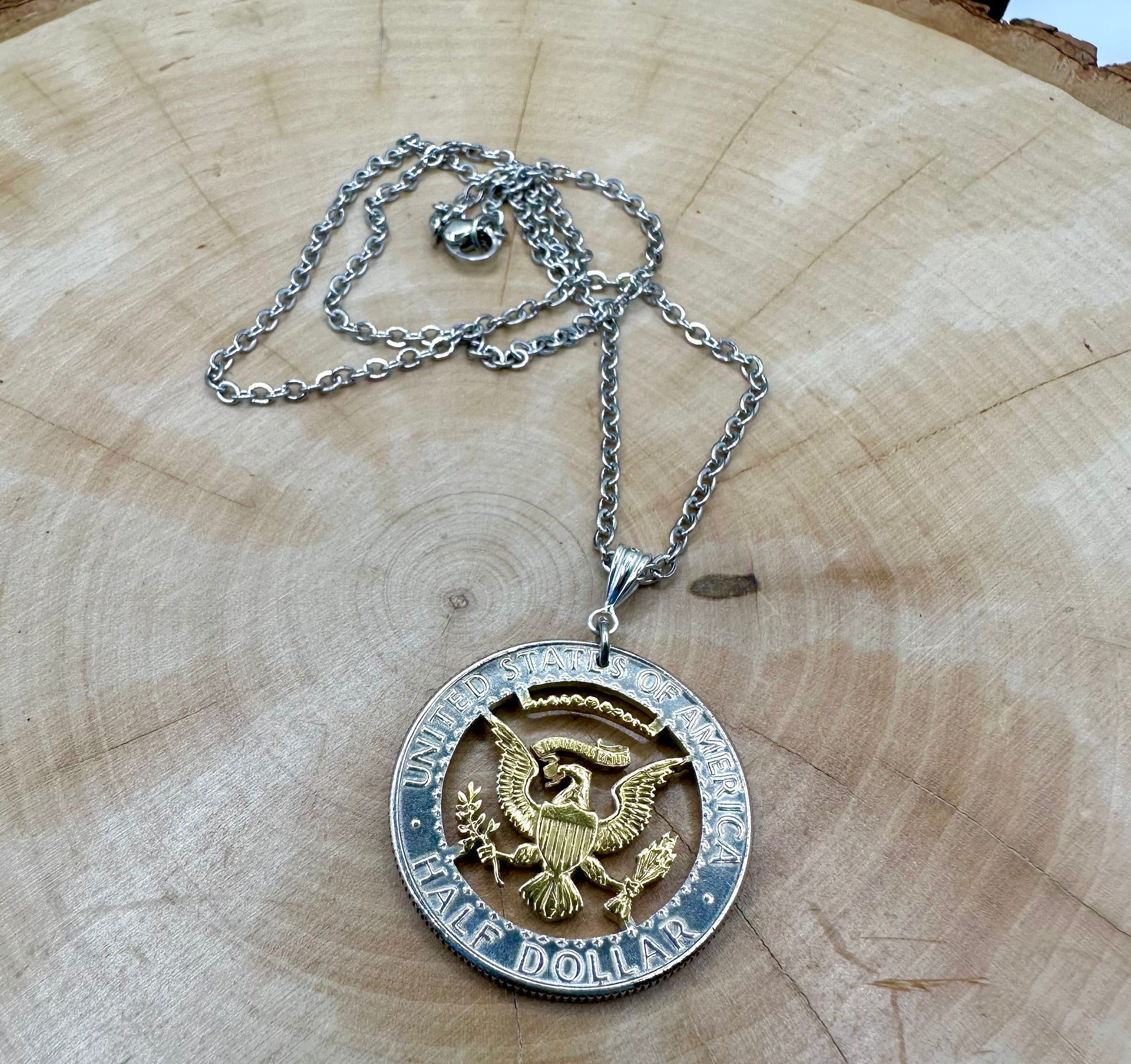 U.S. JFK Eagle Half Dollar Hand Cut Silver Coin Necklace with a 24k gold plated Eagle on a light wood background. - Mountainstruck Coin Jewelry