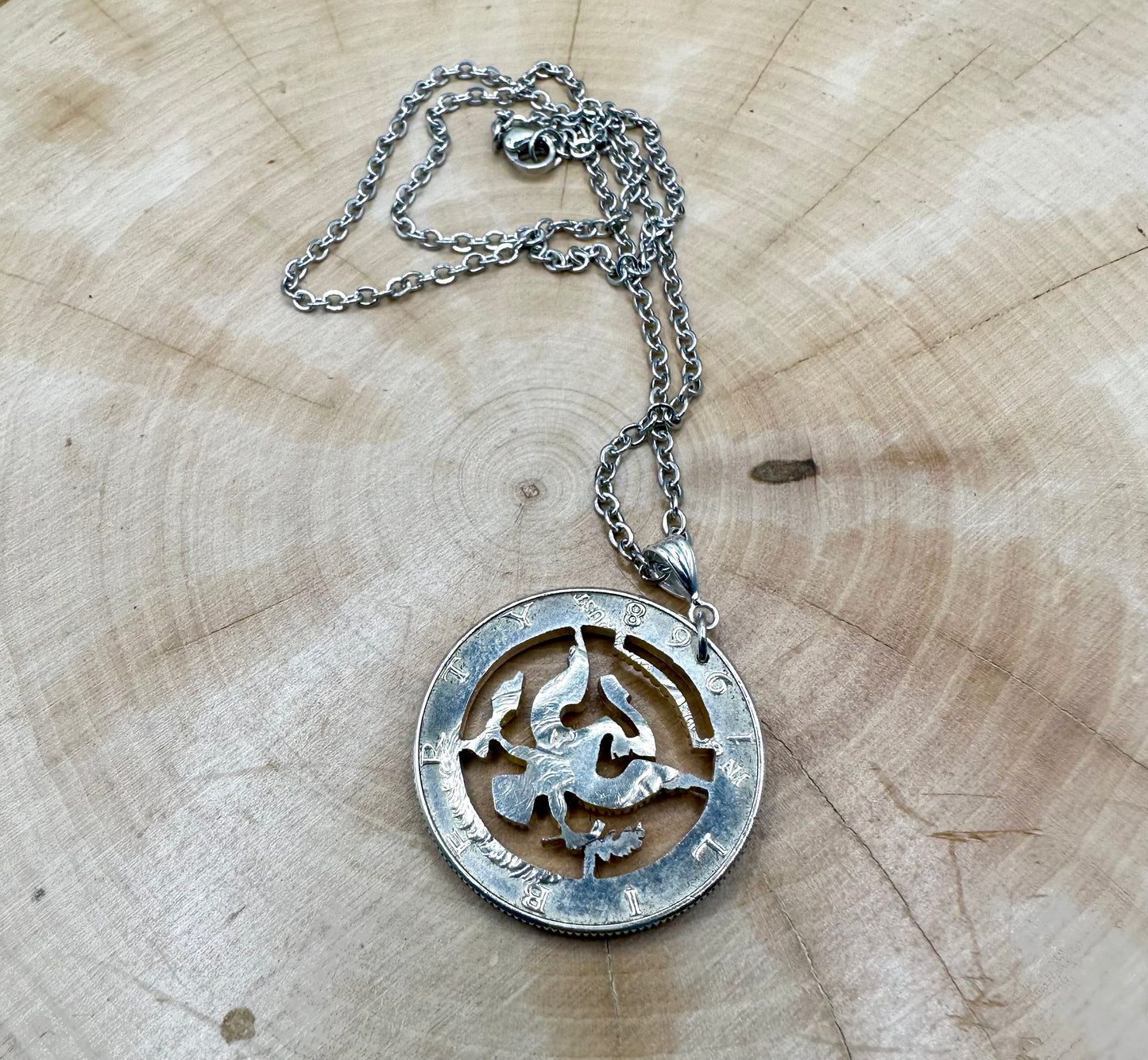 U.S. JFK Eagle Half Dollar Hand Cut Silver Coin Necklace on a light wood background. - Mountainstruck Coin Jewelry