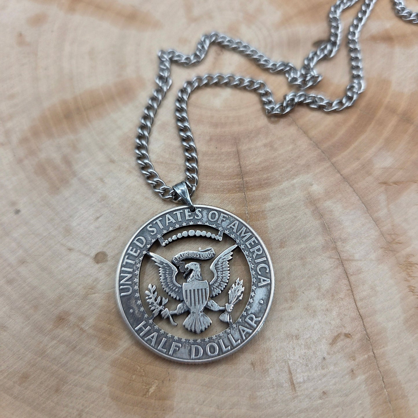 U.S. JFK Eagle Half Dollar Hand Cut Silver Coin Necklace on a light wood background. - Mountainstruck Coin Jewelry