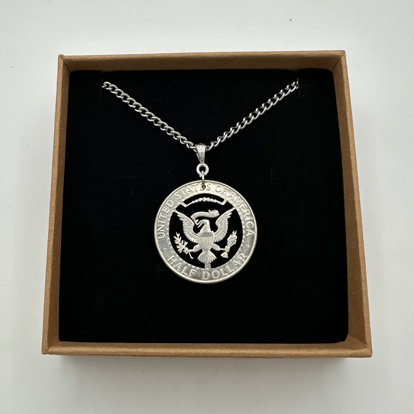 U.S. JFK Eagle Half Dollar Hand Cut Silver Coin Necklace in a brown kraft box on a black velvet background. - Mountainstruck Coin Jewelry