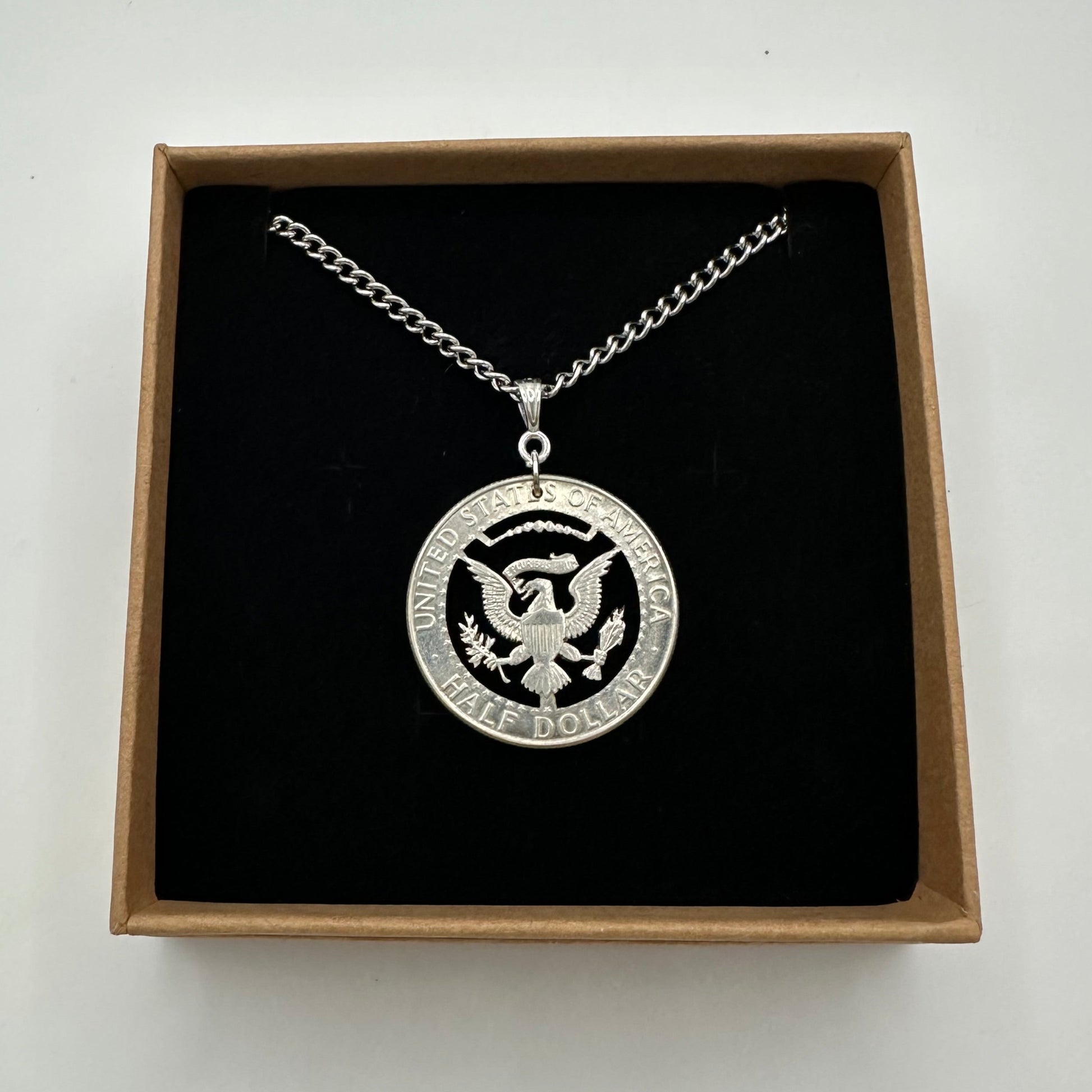 U.S. JFK Eagle Half Dollar Hand Cut Silver Coin Necklace in a brown kraft box on a black velvet background. - Mountainstruck Coin Jewelry