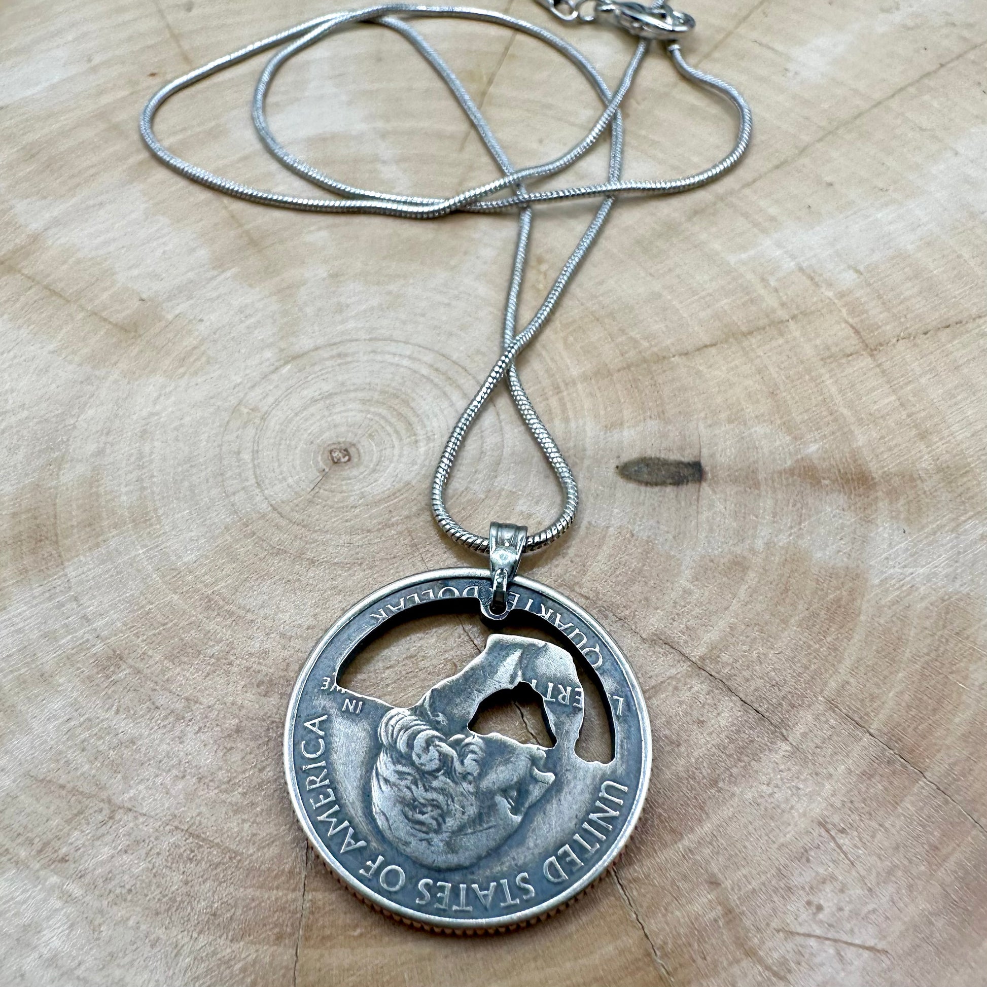 U.S. Arches National Park Hand Cut Coin Necklace back with snake chain on a light wood round. - Mountainstruck Coin Jewelry