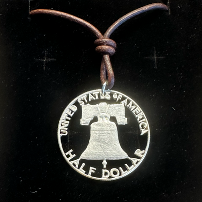 U.S. Cracked Liberty Bell Half Dollar Hand Cut Coin Necklace with a leather cord in a brown kraft box on a black velvet background. - Mountainstruck Coin Jewelry