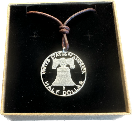 U.S. Cracked Liberty Bell Half Dollar Hand Cut Coin Necklace with a leather cord in a brown kraft box on a black velvet background. - Mountainstruck Coin Jewelry