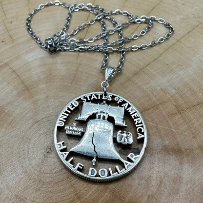 Cracked Liberty Bell U.S. Half Dollar Hand Cut Coin Necklace with stainless chain on a wood background. - Mountainstruck Coin Jewelry