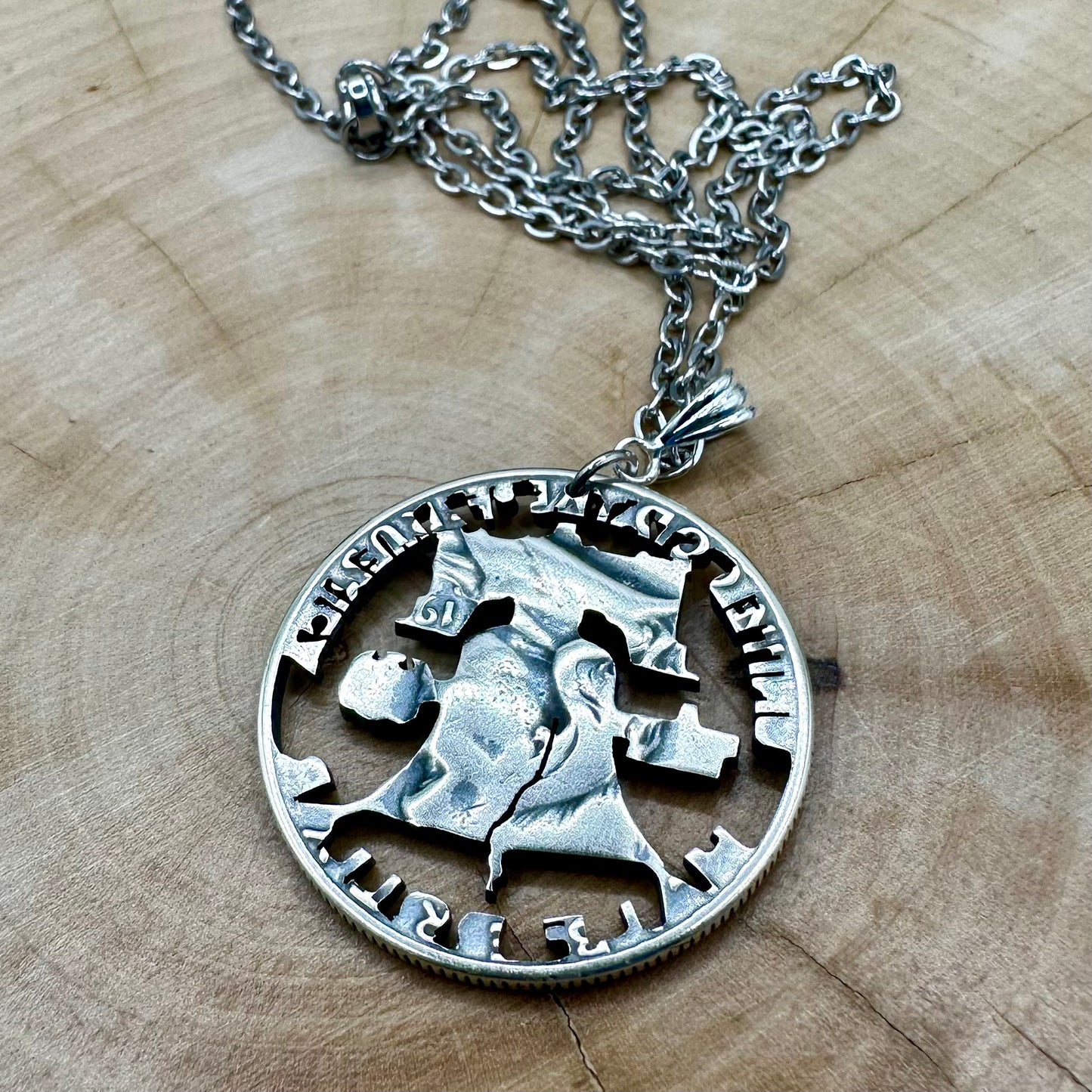Cracked Liberty Bell U.S. Half Dollar Hand Cut Coin Necklace back with stainless chain on a wood background. - Mountainstruck Coin Jewelry