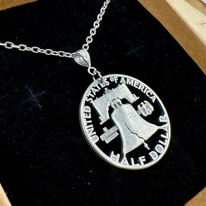 U.S. Cracked Liberty Bell Half Dollar Hand Cut Coin Necklace with a stainless chain in a brown kraft box on a black velvet background. - Mountainstruck Coin Jewelry