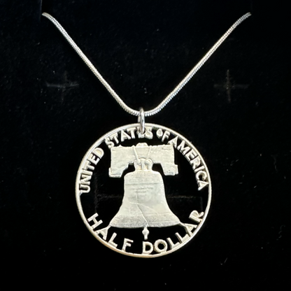 U.S. Cracked Liberty Bell Half Dollar Hand Cut Coin Necklace with a snake chain in a brown kraft box on a black velvet background. - Mountainstruck Coin Jewelry