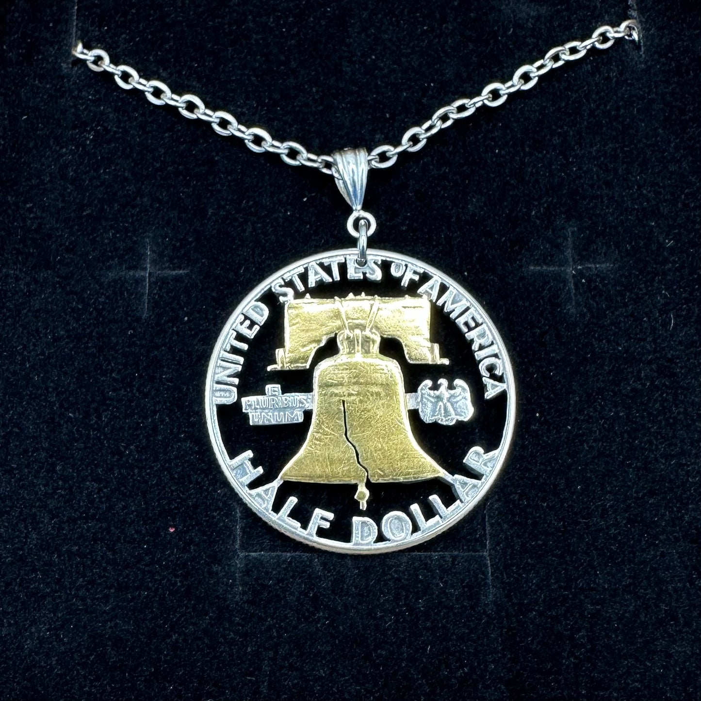 U.S. Cracked Liberty Bell Half Dollar Hand Cut Coin Necklace 24k Gold Plated Bell with a stainless chain on a black velvet background. - Mountainstruck Coin Jewelry