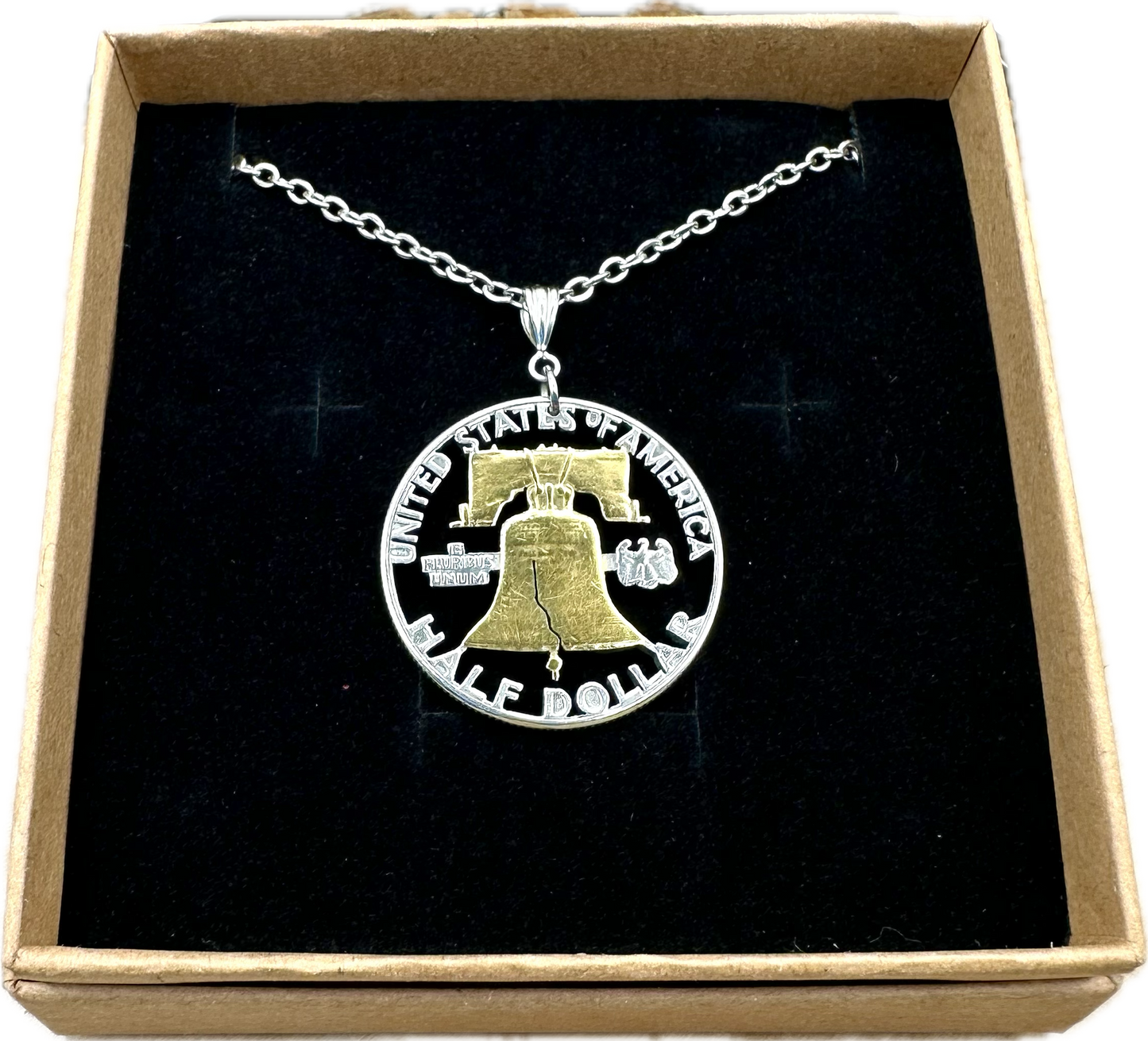 U.S. Cracked Liberty Bell Half Dollar Hand Cut Coin Necklace 24k Gold Plated Bell with a stainless chain in a brown kraft box on a black velvet background. - Mountainstruck Coin Jewelry