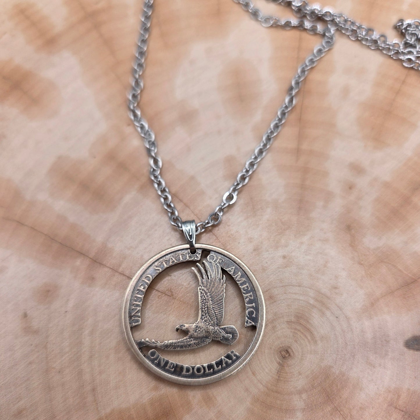 U.S. Flying Eagle Sacagawea One Dollar Hand Cut Coin Necklace on a wood background. - Mountainstruck Coin Jewelry