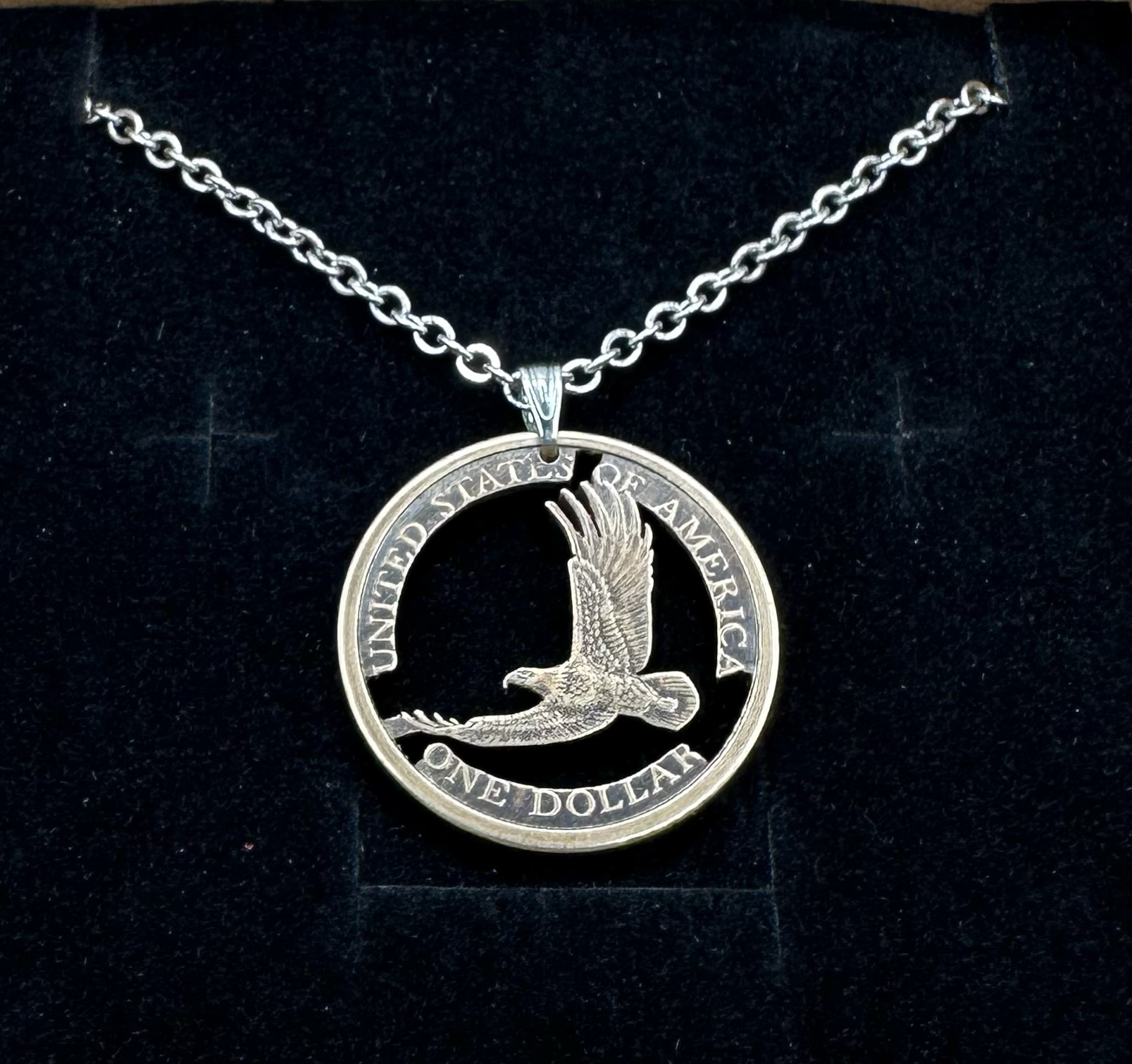 U.S. Flying Eagle Sacagawea One Dollar Hand Cut Coin Necklace with snake chain in a brown kraft box on a black velvet background. - Mountainstruck Coin Jewelry