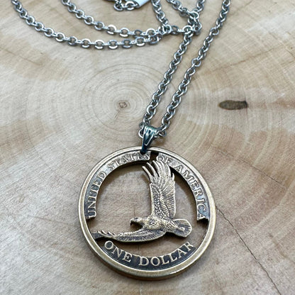 U.S. Flying Eagle Sacajawea One Dollar Hand Cut Coin Necklace with snake chain on a light wood round. - Mountainstruck Coin Jewelry