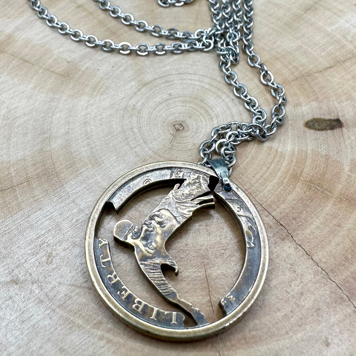 U.S. Flying Eagle Sacajawea One Dollar Hand Cut Coin Necklace with snake chain back on a light wood round. - Mountainstruck Coin Jewelry